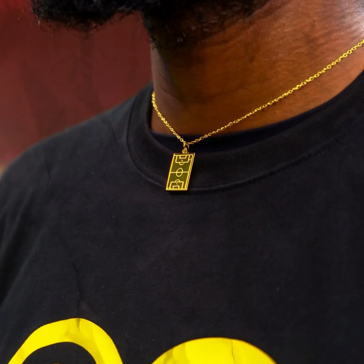 Gold Soccer Field Necklace worn against a club backdrop